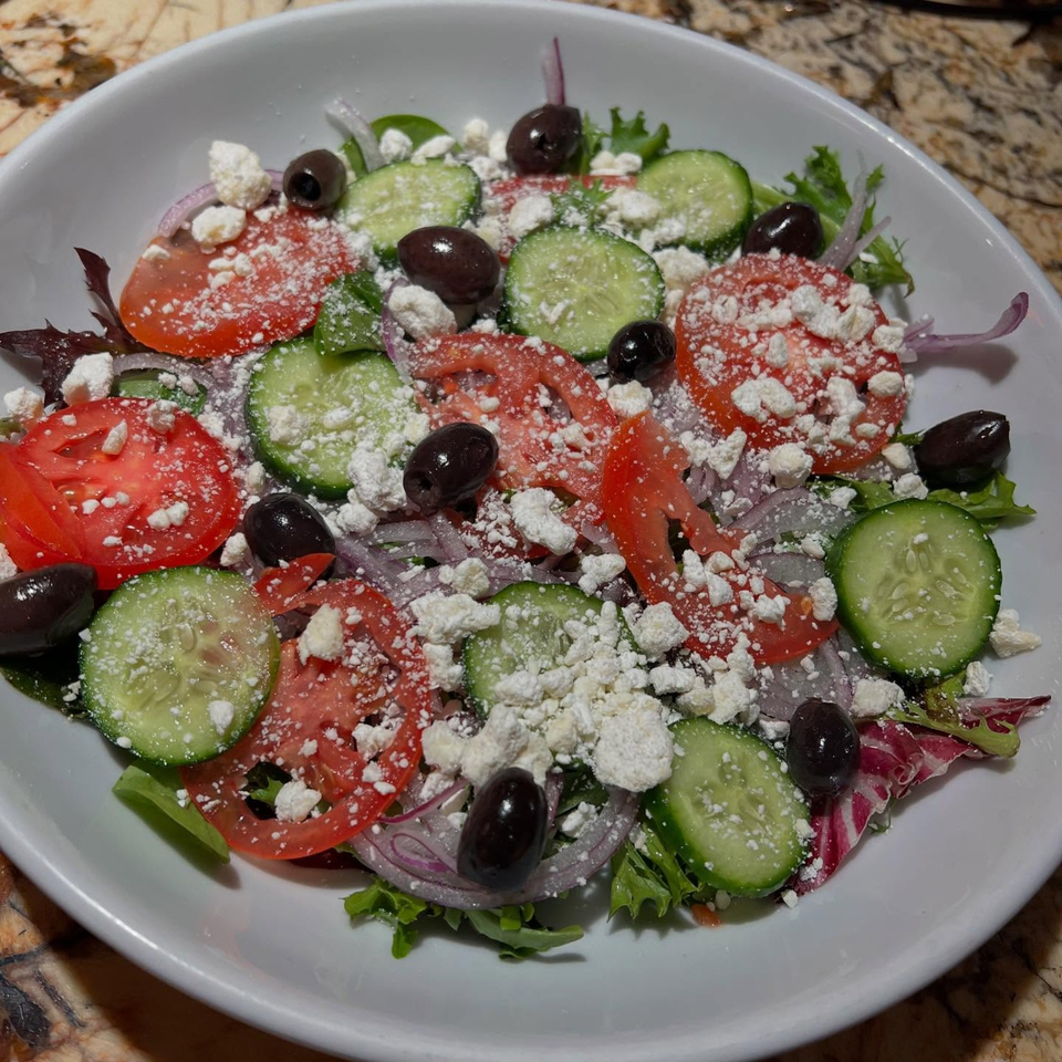 A vibrant Greek salad with tomatoes, cucumbers, olives, red onion, and feta cheese in a white bowl.
