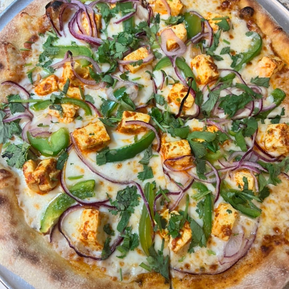 A Slice & Spice paneer pizza with red onions, green peppers, and cilantro.