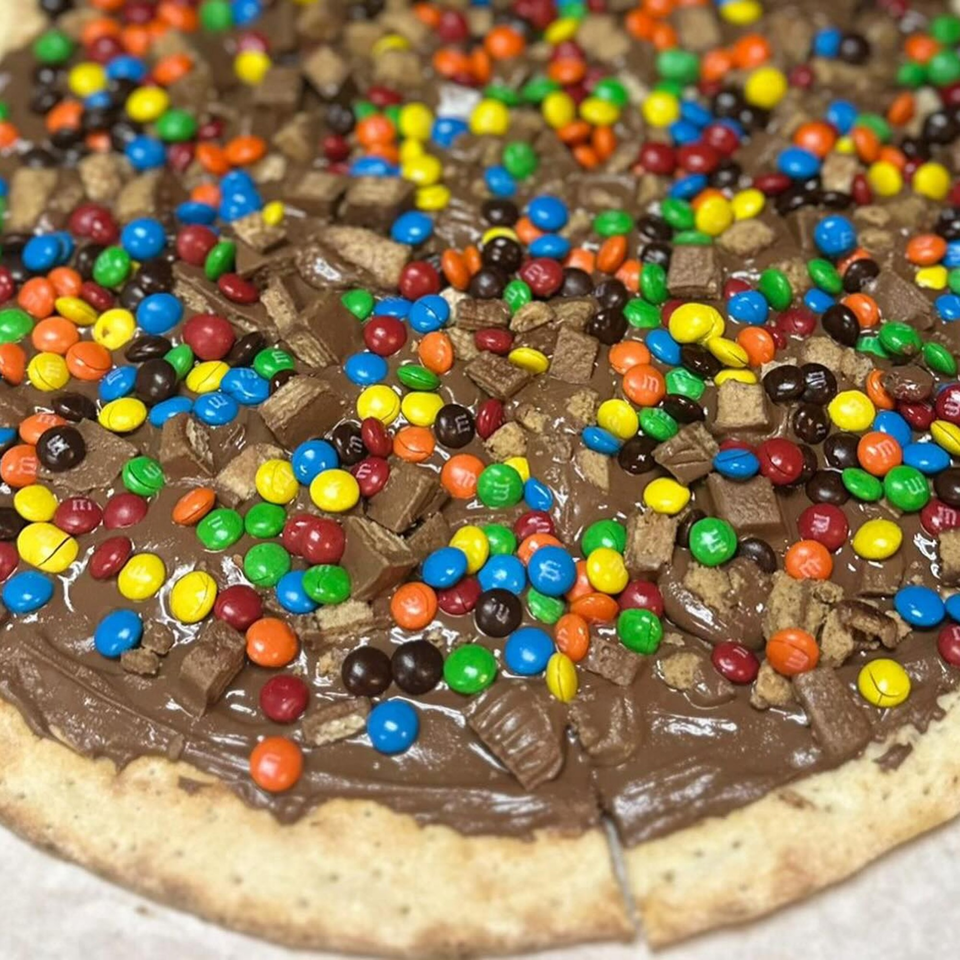 A dessert pizza from Slice & Spice, topped with chocolate spread, colorful candies, and chocolate bar pieces.