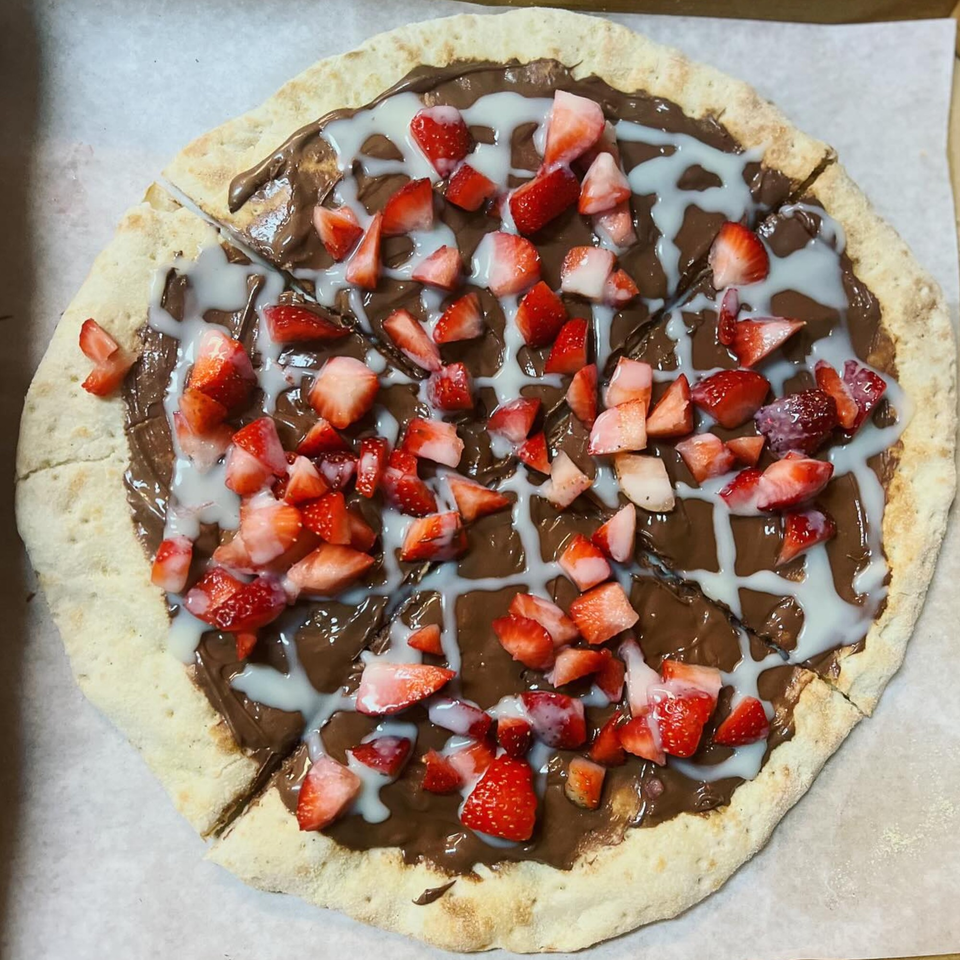 Dessert pizza from Slice & Spice, topped with chocolate spread, white drizzle, and fresh strawberries.