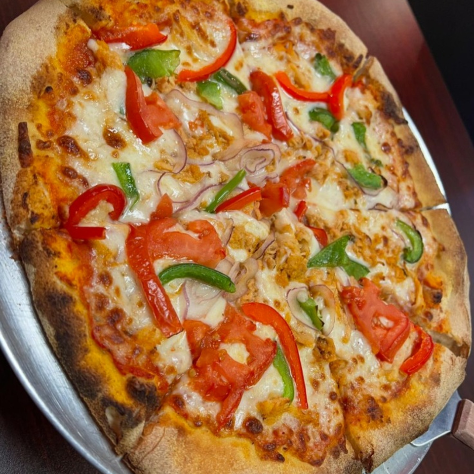 Slice & Spice pizza with red and green peppers, onions, and chicken on a metal tray.