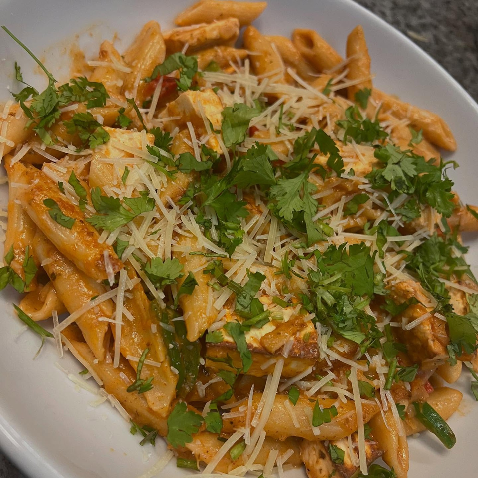 Penne pasta with chicken, red sauce, shredded cheese, and fresh cilantro in a white bowl.